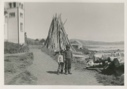 Image of Two native young boys; church and stacked wood beyond